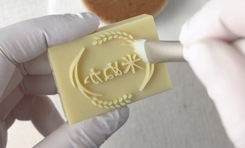 文字の穴や細溝へ垂直に筆を入れて塗布している様子