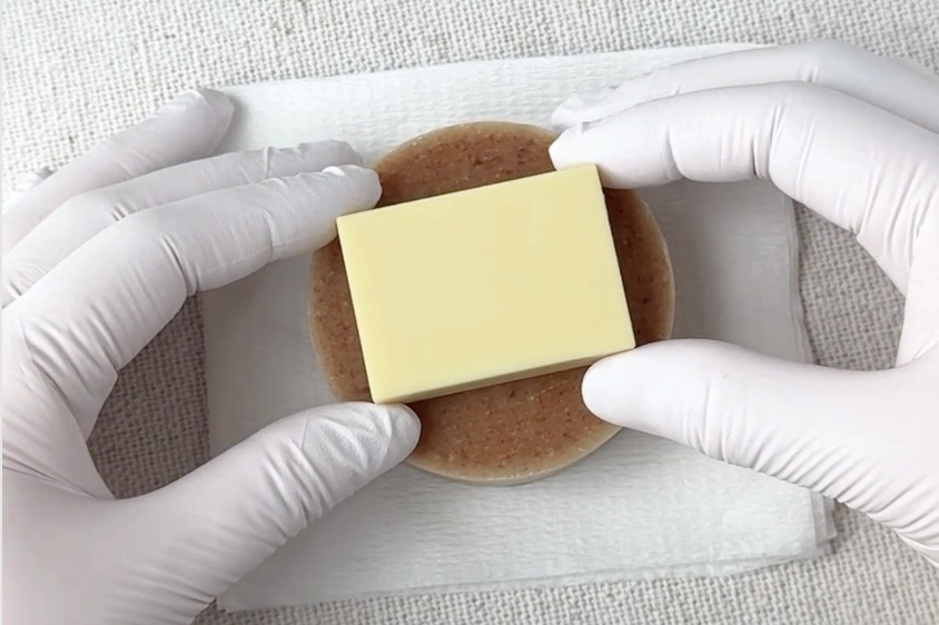 スタンプの印面を軽く触れさせ石鹸の中心位置を合わせている俯瞰ショット